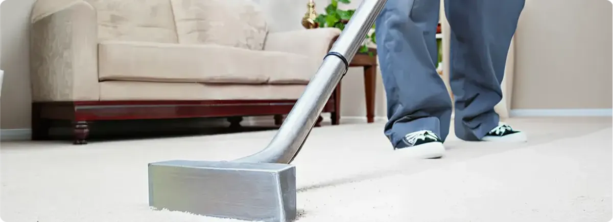 Carpet cleaning technician using a hot-water extraction wand on a light-colored carpet in a living room, Houston, TX.