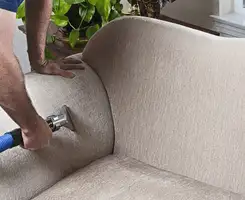 Professional upholstery cleaner deep-cleaning a fabric sofa with a handheld extraction tool and hose in Houston, TX.